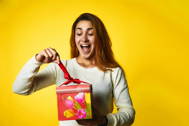Возбужденная рыжая кавказская девушка открывает подарок с удивленным лицом