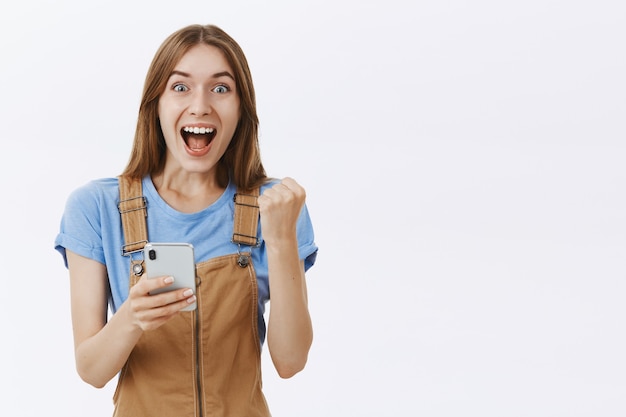 Free photo excited rejoicing beautiful girl reacting to awesome news online, holding smartphone and looking fascinated