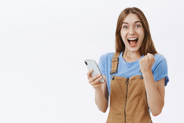 Excited rejoicing beautiful girl reacting to awesome news online, holding smartphone and looking fascinated