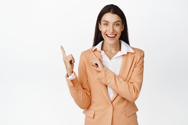 Free photo excited saleswoman pointing fingers at upper left corner smiling while demonstrating company product advertising standing over white background