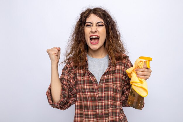 Excited showing yes gesture young cleaning woman holding cleaning agent with rag isolated on white wall