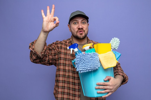 Excited slavic cleaner man holding cleaning equipment and gesturing ok sign 