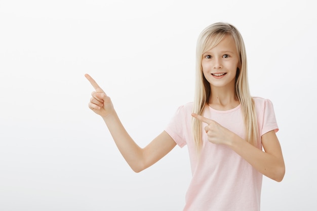 Free photo excited smiling girl asking for something, pointing upper left corner