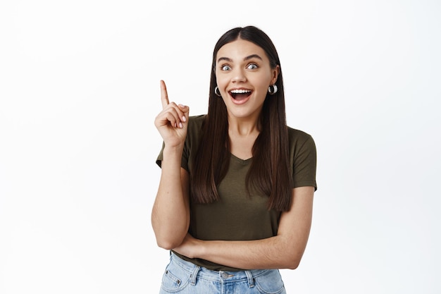 Free photo excited smiling girl have solution, raising index finger and saying suggestion, have good plan, standing against white wall