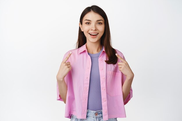 Excited smiling girl pointing fingers at herself looking hopeful standing over white background Copy space