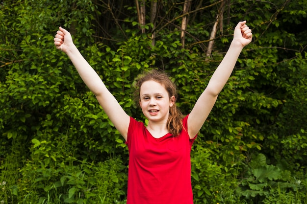 La ragazza sorridente emozionante ha sollevato le mani nel gesto di successo al parco