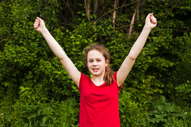 Excited smiling girl raised hands in success gesture at park