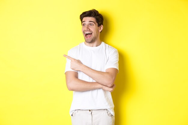Excited smiling man pointing and looking left, checking out promo offer, standing over yellow background.