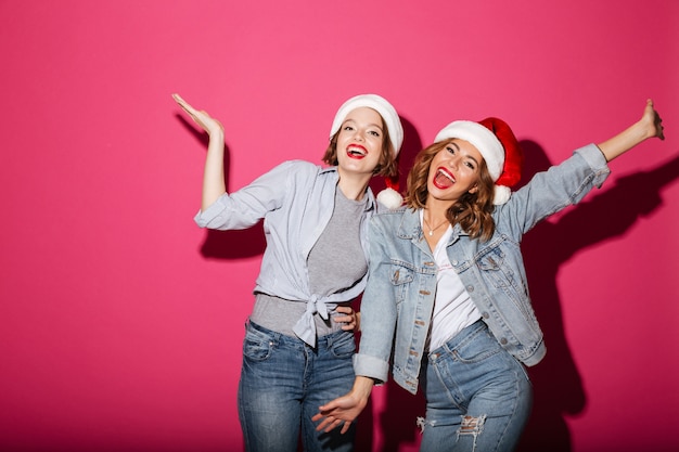 Due amici sorridenti emozionanti delle donne che indossano i cappelli di santa di natale