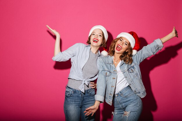 Excited smiling two women friends wearing christmas santa hats