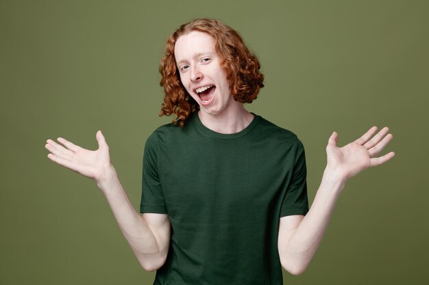 Excited spreading hands young handsome guy wearing green t shirt isolated on green background