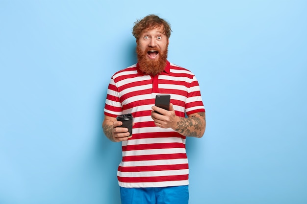 Excited stylish ginger guy posing against the blue wall