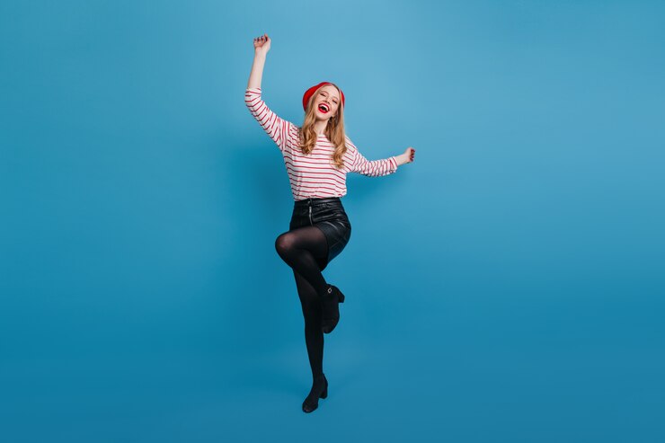 Free Photo excited stylish girl dancing on blue wall. full length view of pleasant blonde lady in black skirt.