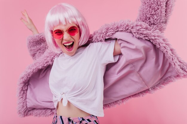 선글라스와 분홍색 벽에 포즈가 발에 흥분된 세련 된 소녀. 행복 한 젊은 여자 춤과 웃음