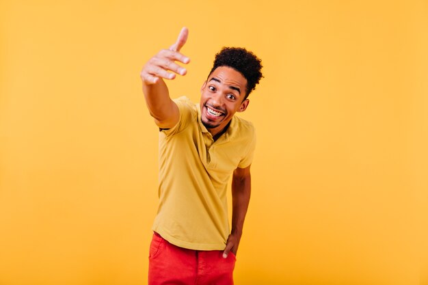 Eccitato uomo alla moda con i capelli corti agitando la mano. ritratto dell'interno del ragazzo africano che ride positivo.