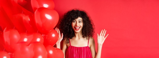 Free photo excited stylish woman with curly hair wearing dress raising hands up and laughing happy standing nea