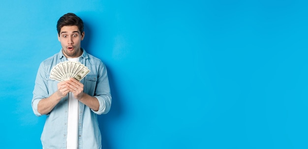 Foto gratuita eccitato uomo di successo che conta soldi guardando soddisfatto in contanti e sorridendo in piedi sopra il dorso blu