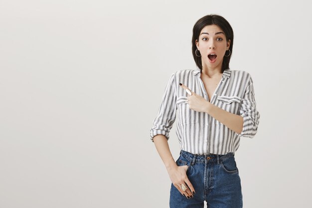 Excited surprised attractive woman pointing finger upper left corner at awesome announcement