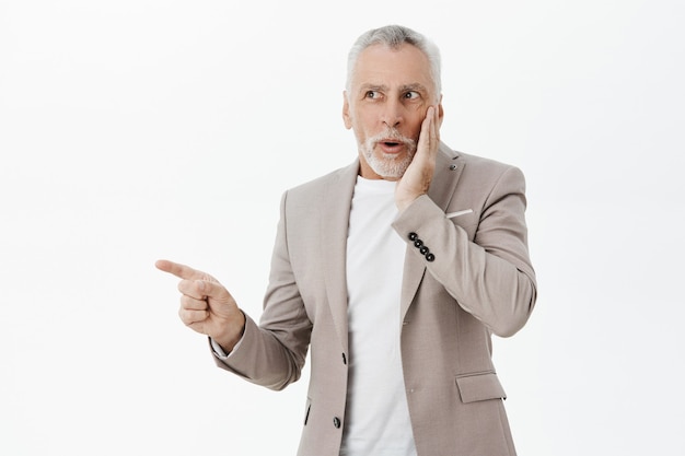 Excited and surprised elderly man in suit pointing and looking left