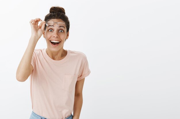 Excited and surprised pleased young beautiful woman with tan and messy hairbun taking off glasses