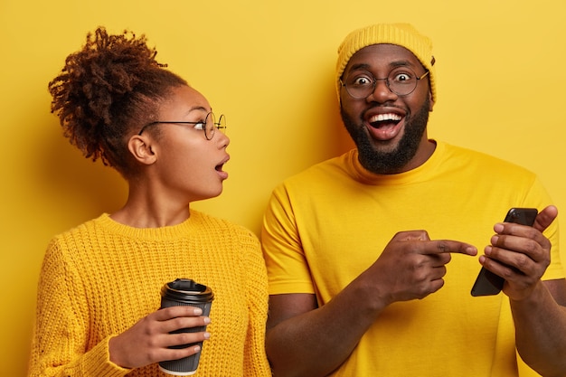 Excited surprised woman listens with great interest male model who tells about great opportunities and functions of new smartphone