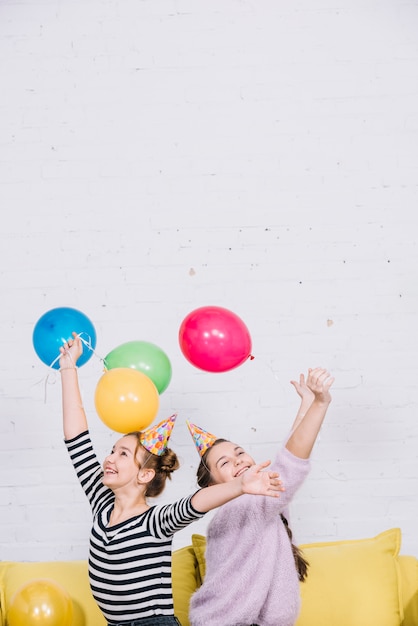 Excited teenage girls raising their hands holding colorful balloons