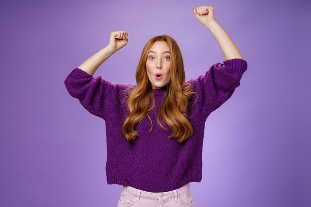 Excited and thrilled woman reacting to unexpected goal raising hands in wave gesture folding lips inhaling breath to scream yes and wow being impressed, triumphing from success and good news.