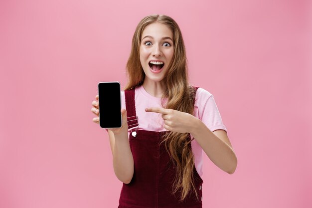 Excited and thrilled young teenage girl in overalls and tshirt smiling amazed full of happiness poin...