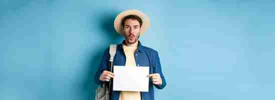 Free photo excited tourist in straw hat holding empty piece of paper and looking amused going on summer travel