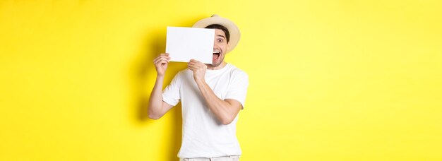 Excited tourist on vacation showing blank piece of paper for your logo holding sign near face and sm