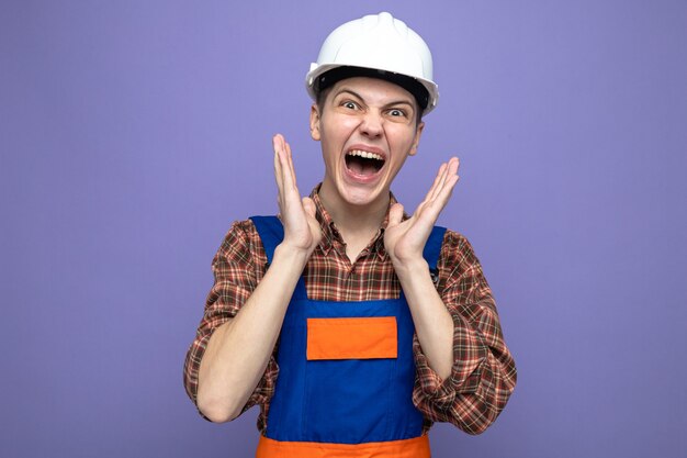 Excited with hands around face young male builder wearing uniform