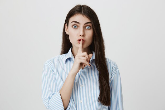 Excited woman asking keep silent, shushing with index finger pressed to lips