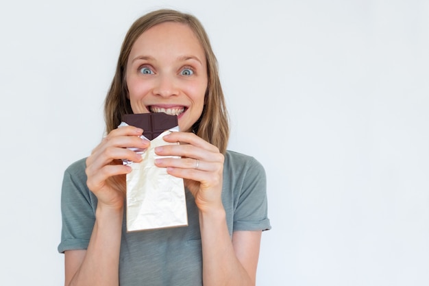 Free photo excited woman eating chocolate bar in gold foil