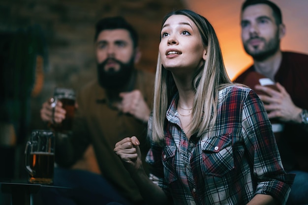Excited woman and her friends cheering for their team while watching sports match on TV at home