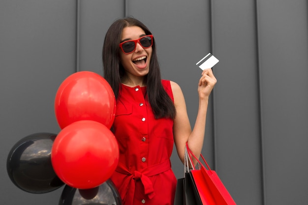 Excited woman holding balloons and shopping card