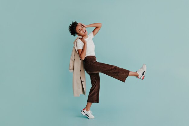 Excited woman in pants dancing on turquoise wall