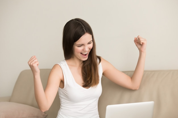 Excited woman says yes while looking on laptop