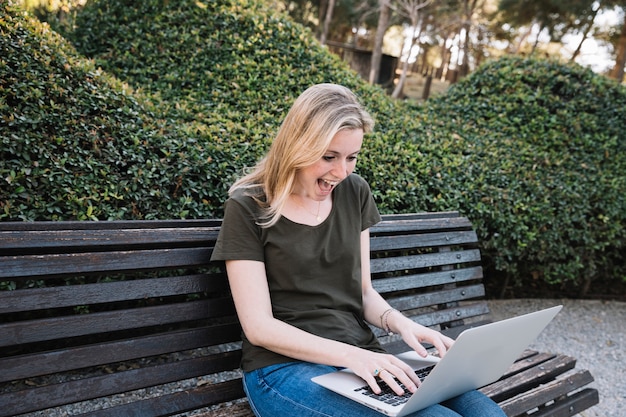 Excited woman using laptop in park