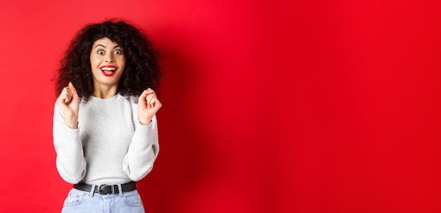 Free photo excited woman winning prize rejoicing and looking happy smiling amazed standing against red backgrou