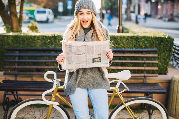 Excited woman with newspaper near bicycle