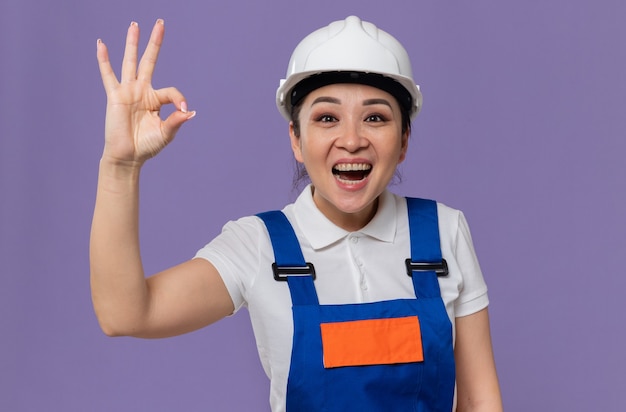 Excited young asian builder woman with white safety helmet gesturing ok sign 