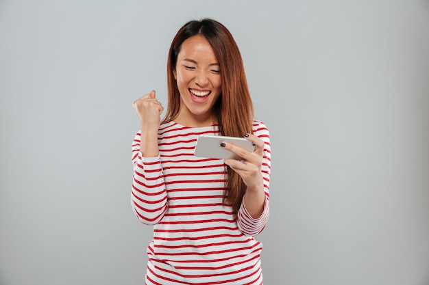 Excited young asian lady play games by phone