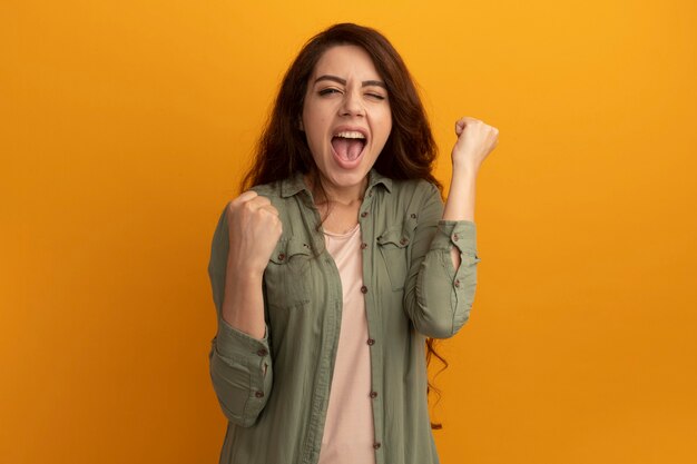 Excited young beautiful girl wearing olive green t-shirt showing yes gesture isolated on yellow wall