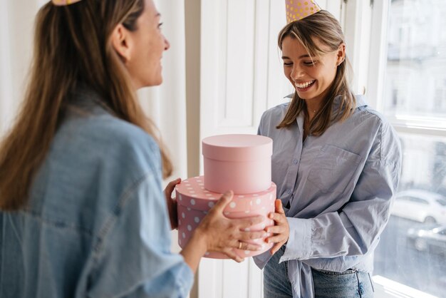 Excited young blonde caucasian woman receiving gift from her friend indoors. Concept of celebration, happiness and emotions.