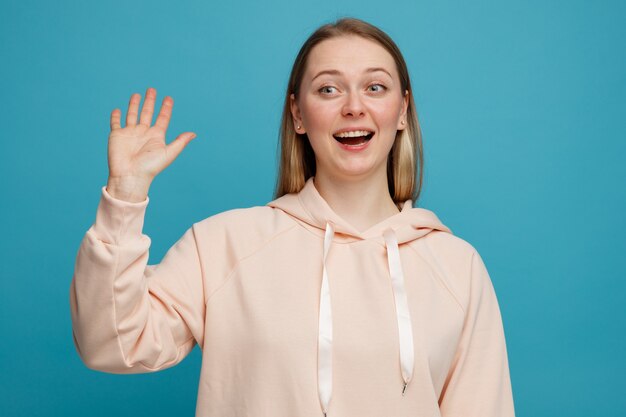Excited young blonde woman looking at side doing hi gesture 