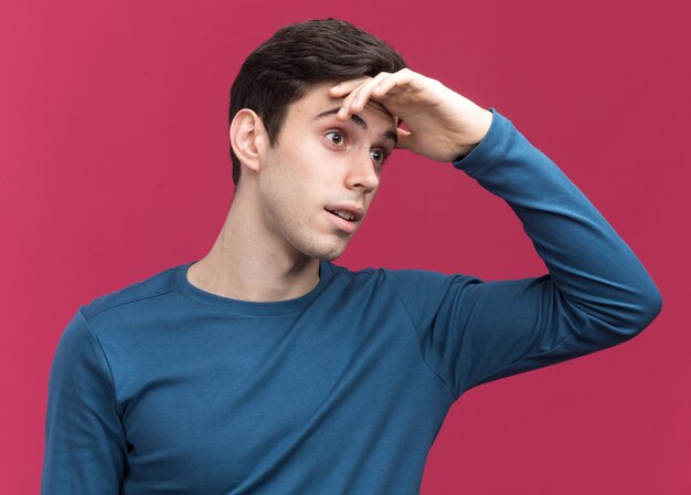 Excited young brunette caucasian boy puts hand on forehead and looks at side