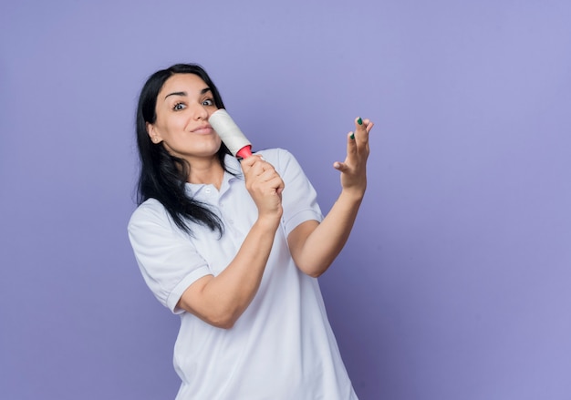 Excited young brunette caucasian girl holds sticky brush and raises hand isolated on purple wall