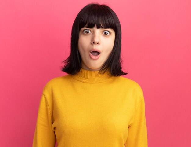 Excited young brunette caucasian girl looks at camera isolated on pink wall with copy space