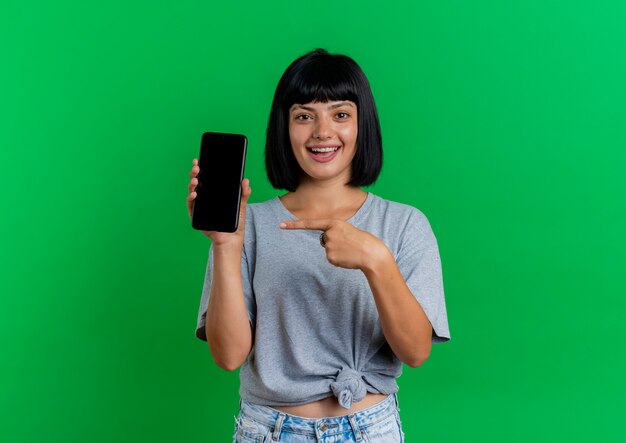 Excited young brunette caucasian woman holds and points at phone