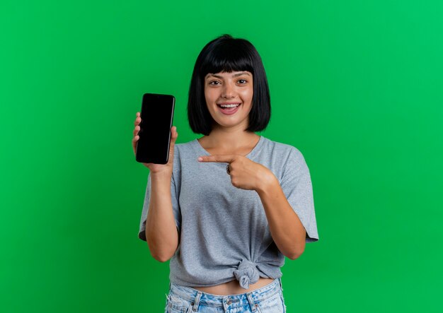 Возбужденная молодая брюнетка кавказская женщина держит и указывает на телефон